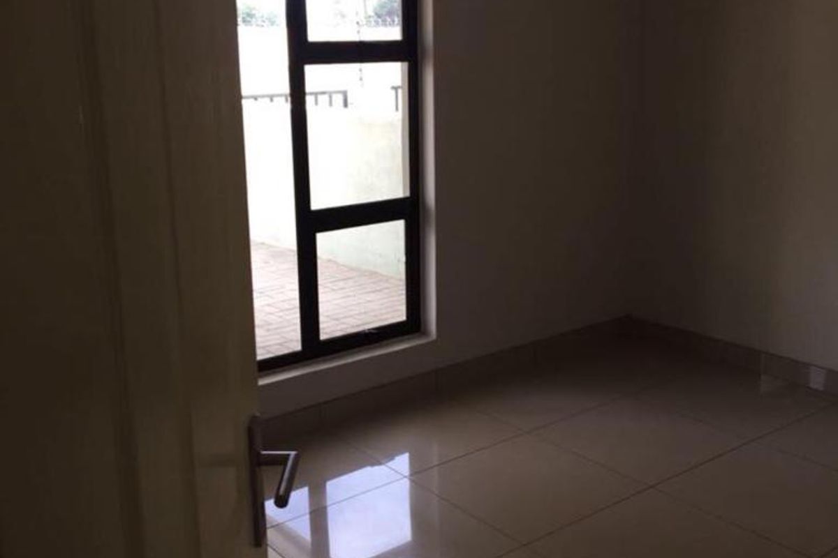 A vacant bedroom featuring neutral tiled flooring and a large aluminium-framed window, providing a clean and blank canvas for interior design.