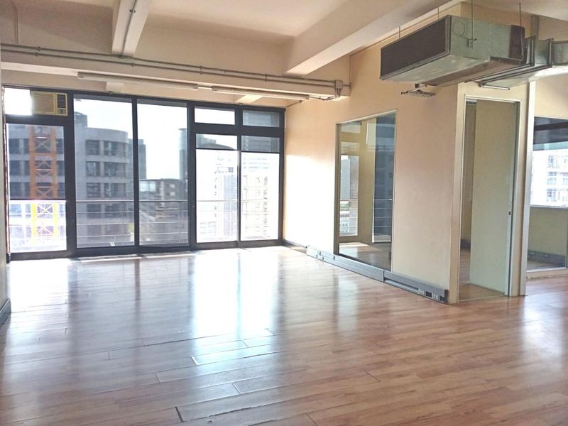 Spacious open-plan office area featuring laminate flooring, exposed industrial-style ceiling beams, HVAC ducting, and large glass sliding doors providing ample natural light.