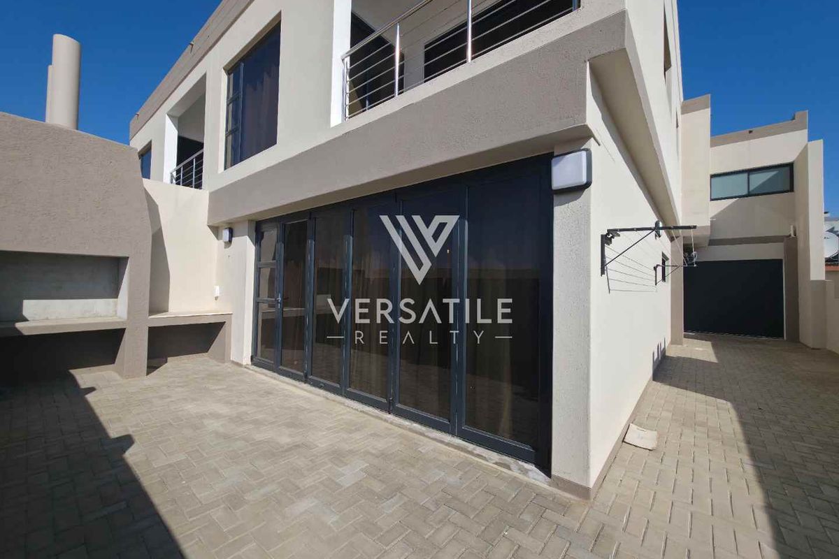 Rear exterior view featuring a paved patio area, built-in braai, and large folding glass doors leading into the home.