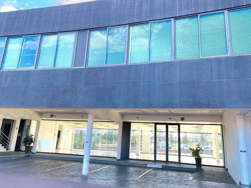 Modern retail storefront featuring large glass display windows, aluminum framing, and a covered parking area with designated bays.