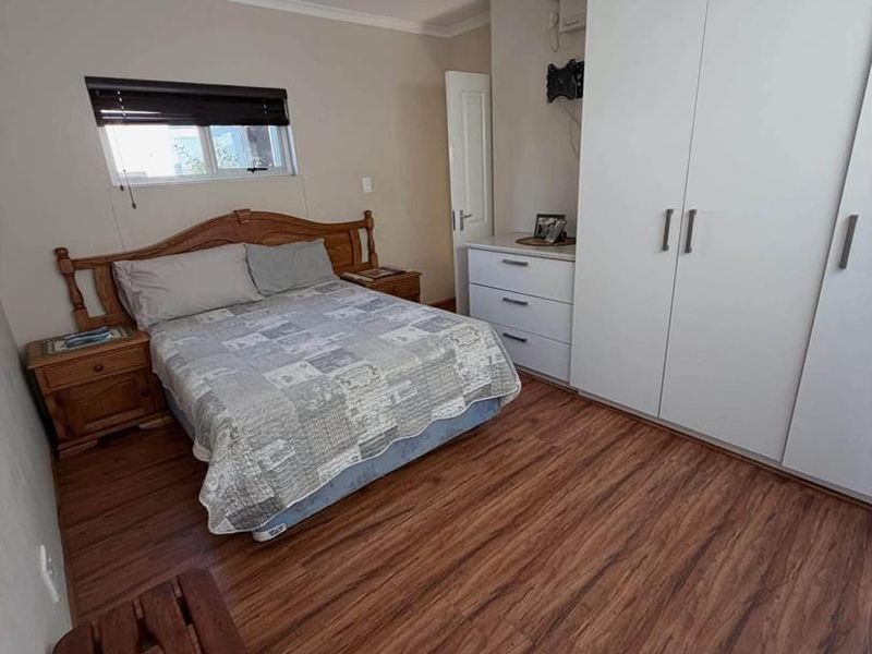 A functional bedroom featuring laminate flooring, a built-in wardrobe, and a window, providing a clean and practical living space.