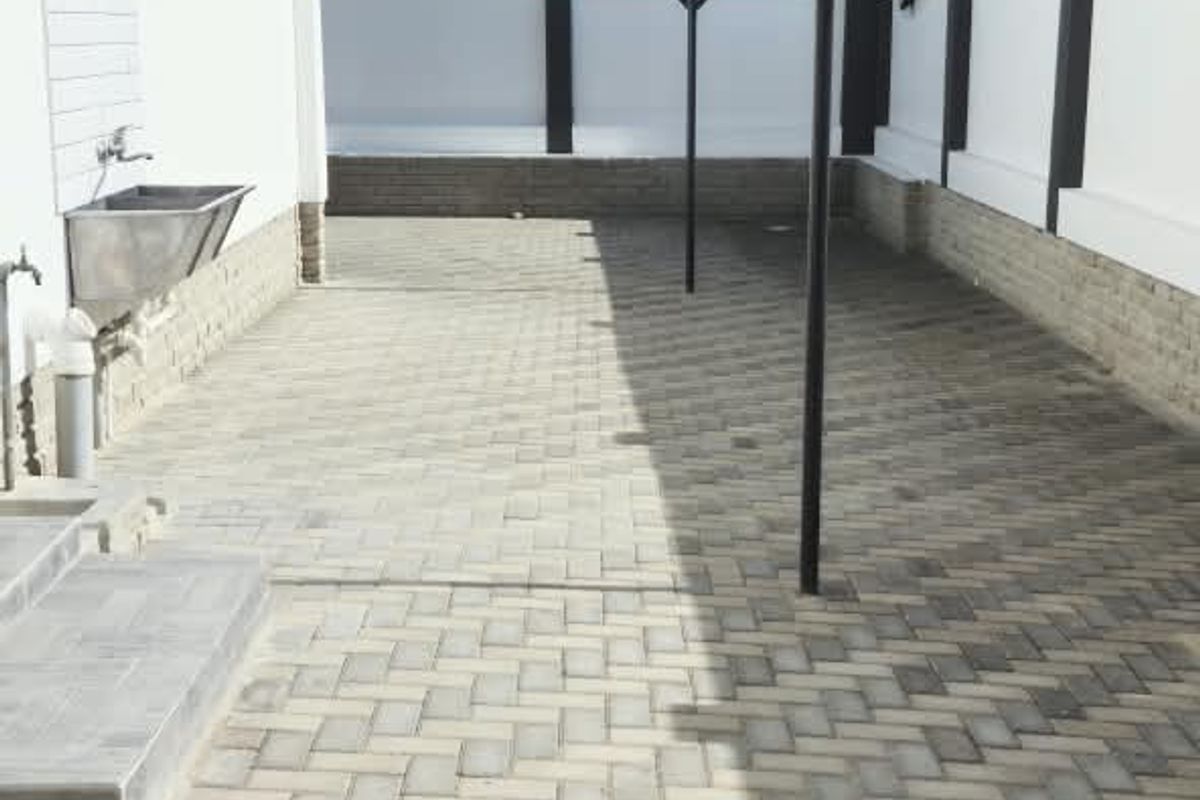 A clean, paved rear courtyard featuring a wall-mounted utility sink and fixed clothesline, enclosed by a perimeter boundary wall.