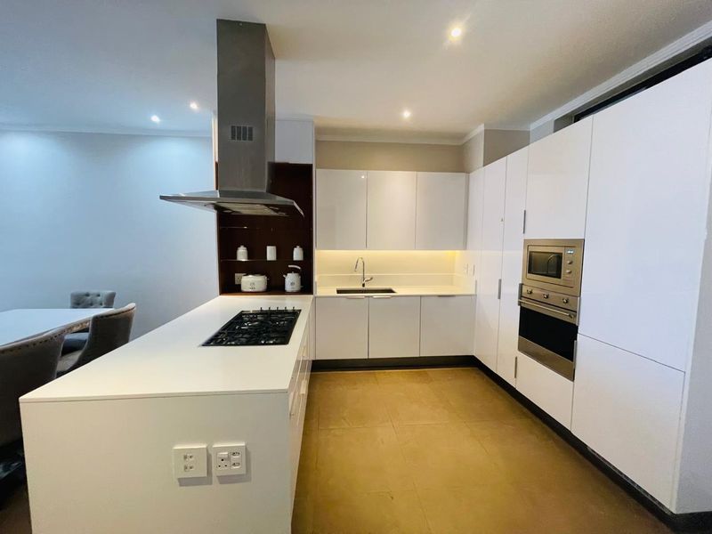 Modern kitchen featuring sleek white cabinetry, a central island with a gas hob, integrated appliances, and warm under-cabinet lighting.