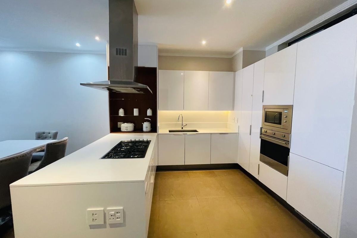 Modern kitchen featuring sleek white cabinetry, a central island with a gas hob, integrated appliances, and warm under-cabinet lighting.