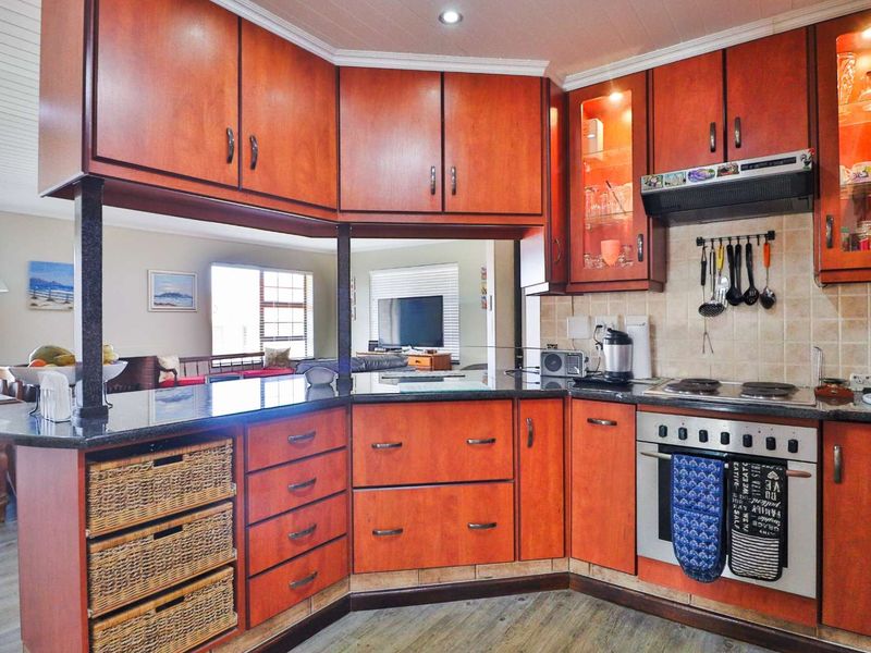 A functional kitchen featuring timber cabinetry, granite countertops, a built-in oven with hob, and an extractor fan, with an open-plan layout to the living area.