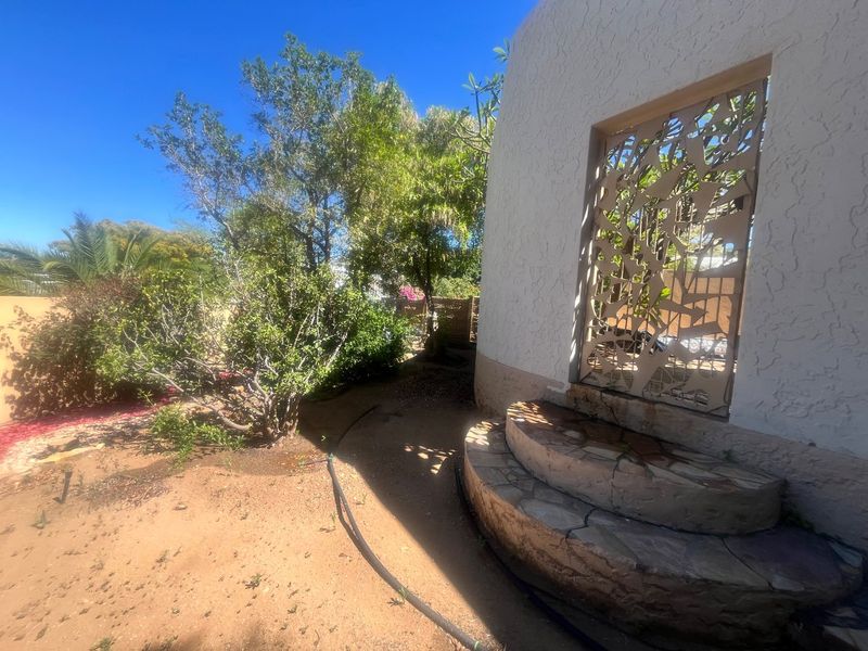 Rear garden area featuring a decorative metal security gate, textured stucco wall, and stone-clad curved steps leading to an entrance.