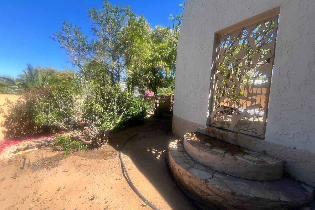 Rear garden area featuring a decorative metal security gate, textured stucco wall, and stone-clad curved steps leading to an entrance.
