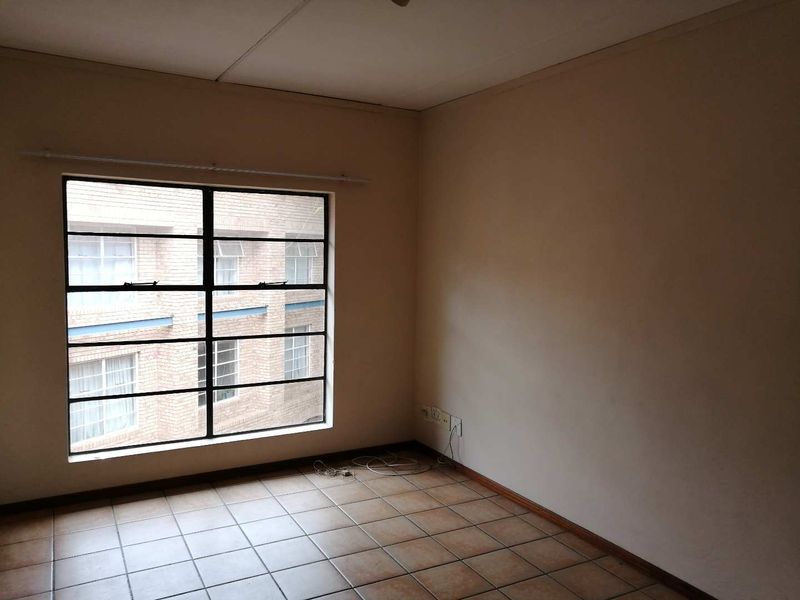 An empty bedroom featuring tiled flooring and a large steel-framed window, offering a blank canvas for renovation or interior design.