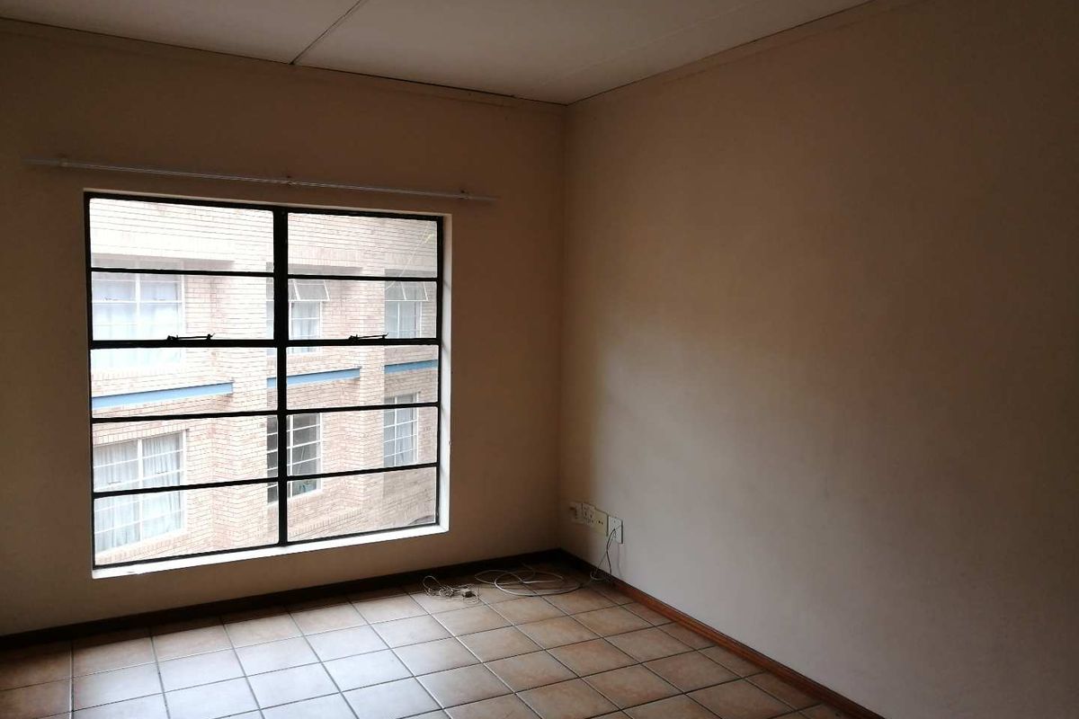An empty bedroom featuring tiled flooring and a large steel-framed window, offering a blank canvas for renovation or interior design.