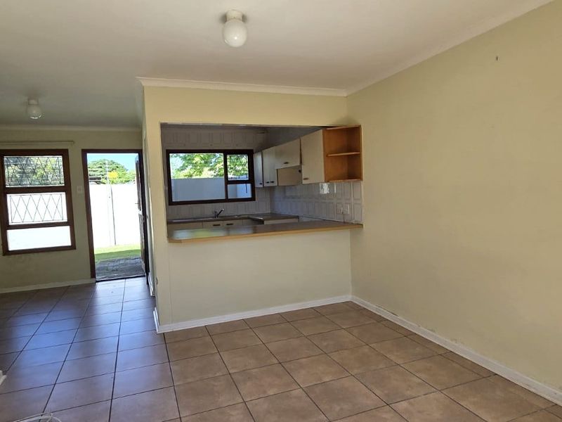 An open-plan living and kitchen area featuring tiled floors, built-in cabinetry, and a breakfast counter, requiring cosmetic updates to the walls.