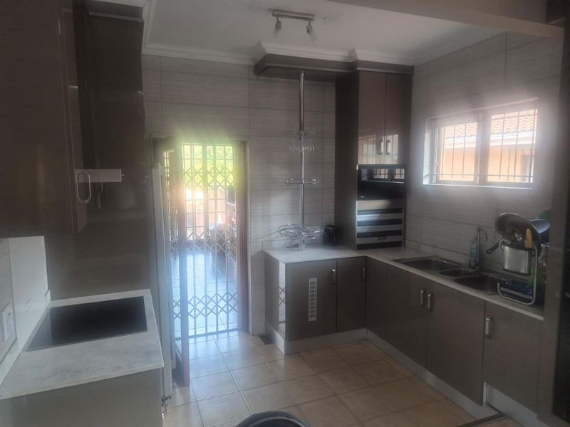 Modern kitchen featuring sleek cabinetry, integrated oven, hob, and double sink, with tiled finishes and direct access to an outdoor area via security gate.