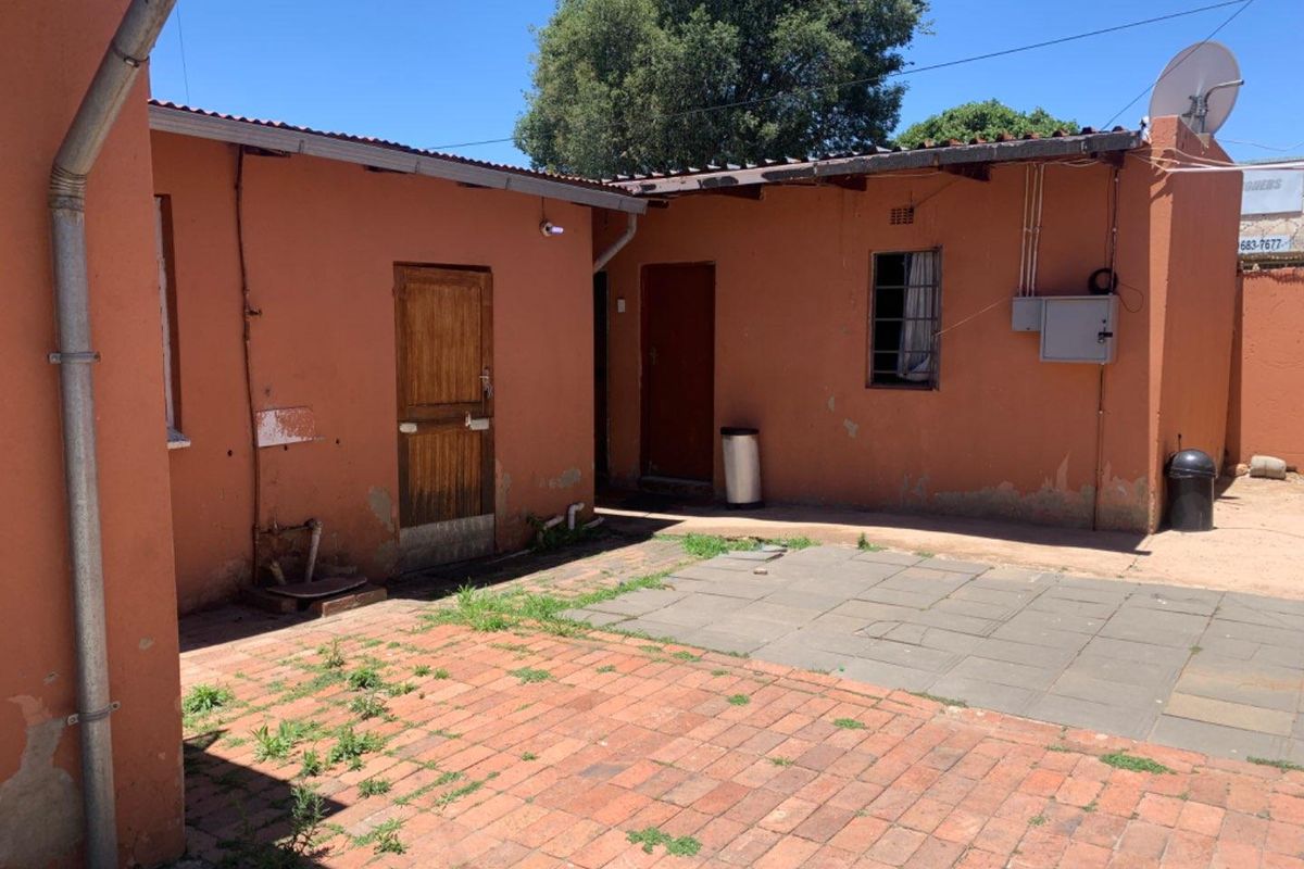 Rear exterior view of the property featuring a paved courtyard area, brick walls, and access doors.