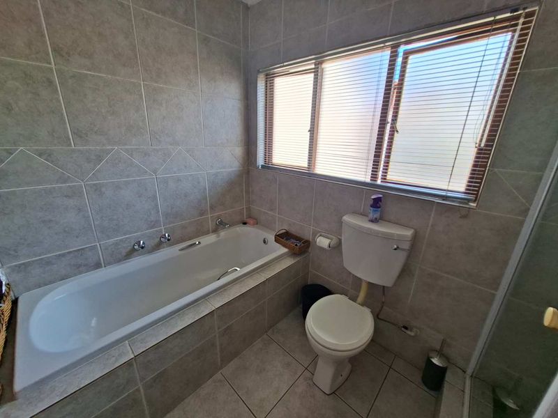 A functional bathroom featuring full-height ceramic wall tiling, a built-in bathtub, and a standard toilet, complemented by natural light from a window.