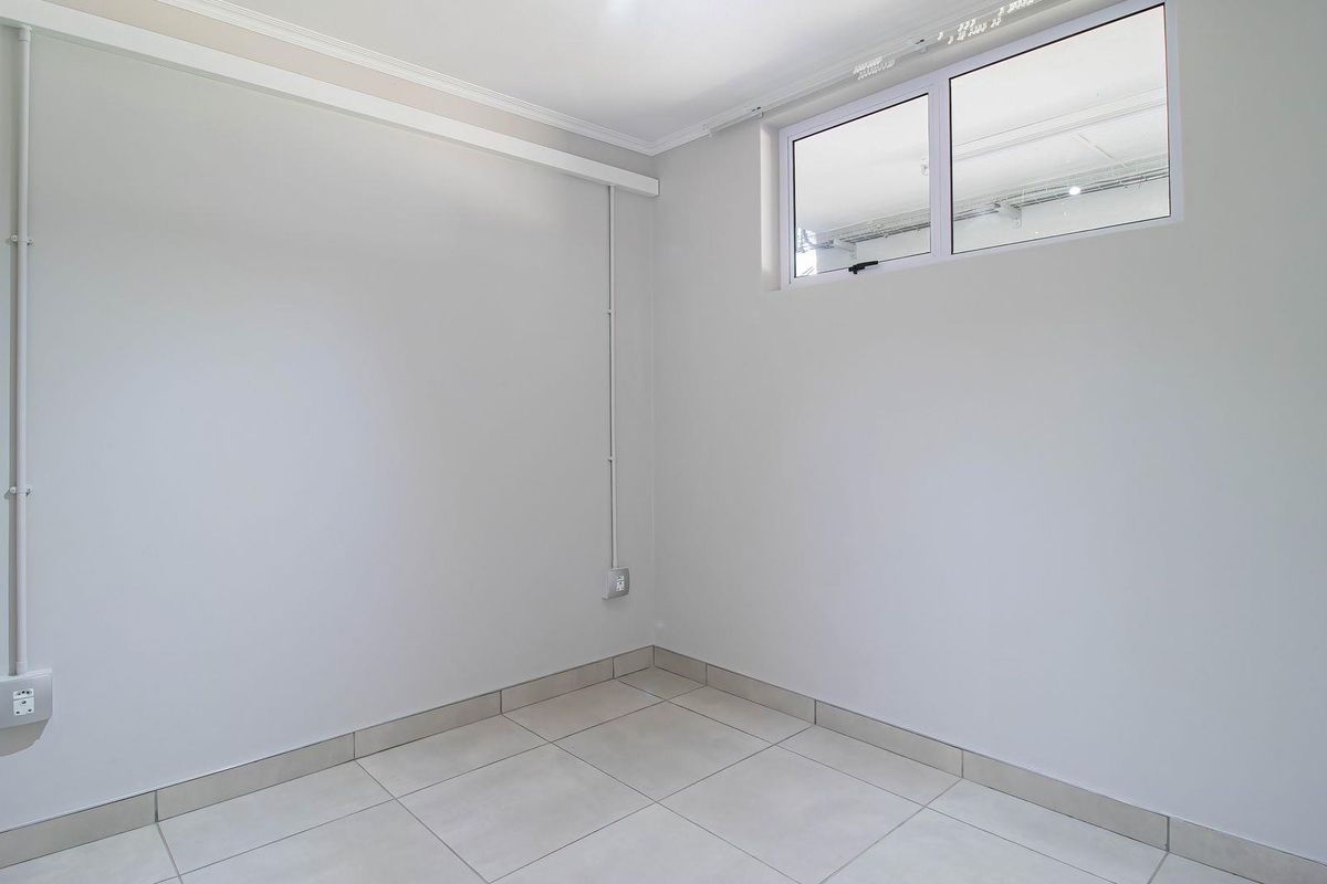 A clean, empty bedroom featuring neutral tiled flooring, white walls, and a high-level window providing natural light.