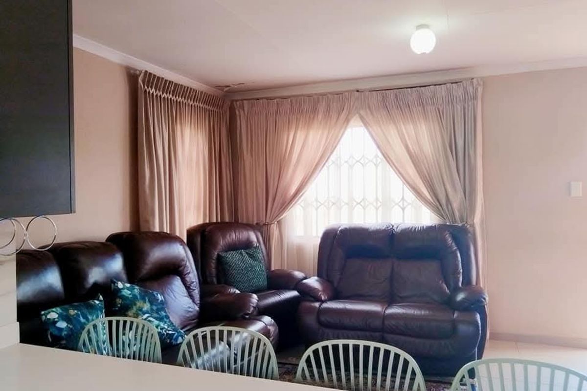 A living area featuring neutral walls, curtained windows with security bars, and a ceiling light fixture, providing a comfortable and functional space.