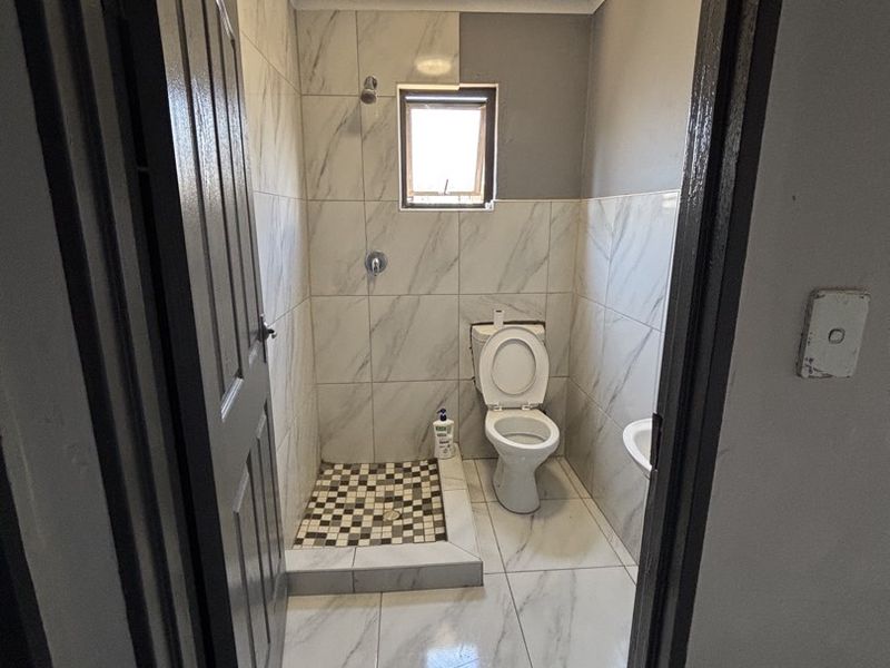 A compact bathroom featuring a walk-in shower with mosaic floor tiles, a toilet, and marble-effect wall and floor tiles.