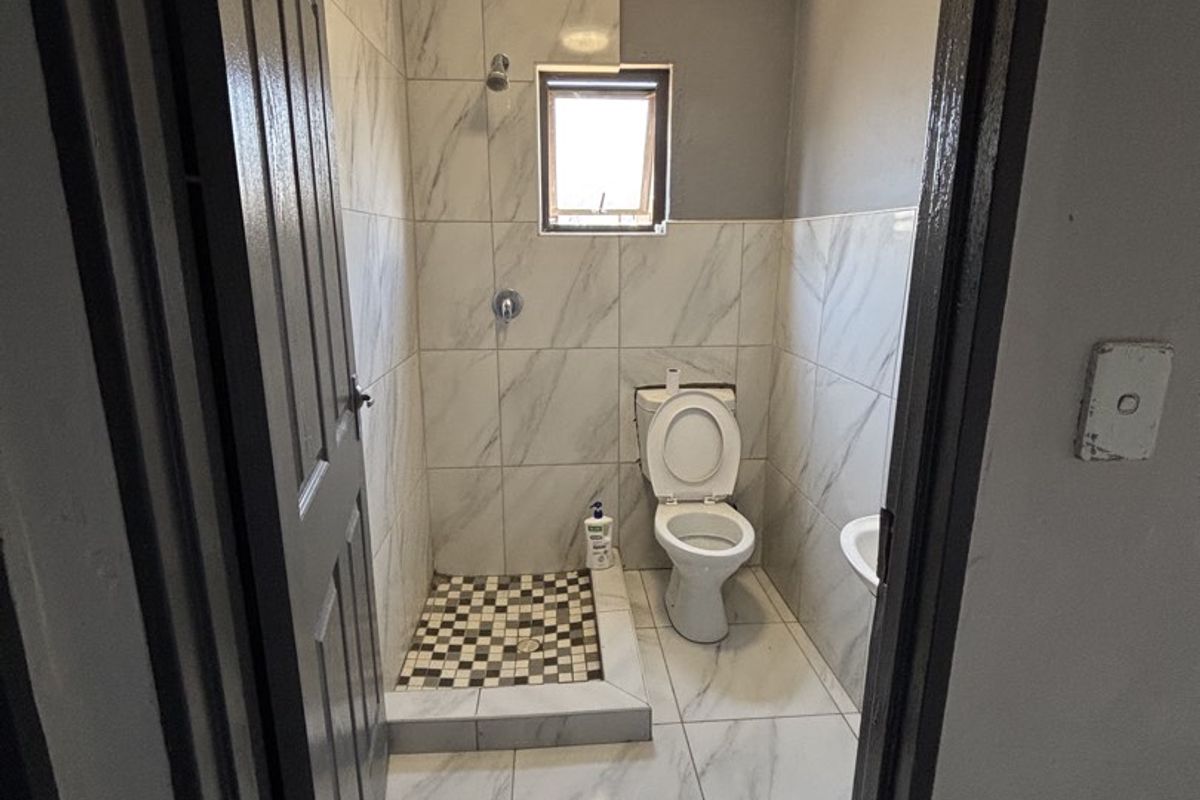 A compact bathroom featuring a walk-in shower with mosaic floor tiles, a toilet, and marble-effect wall and floor tiles.