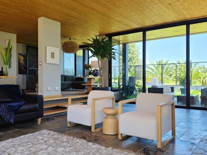 Spacious living area featuring a warm timber-clad ceiling, natural stone flooring, and expansive floor-to-ceiling glass doors that provide seamless indoor-outdoor flow.