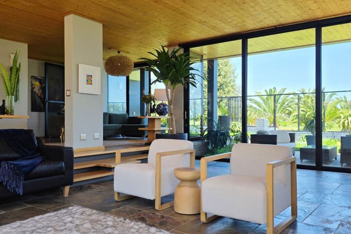 Spacious living area featuring a warm timber-clad ceiling, natural stone flooring, and expansive floor-to-ceiling glass doors that provide seamless indoor-outdoor flow.
