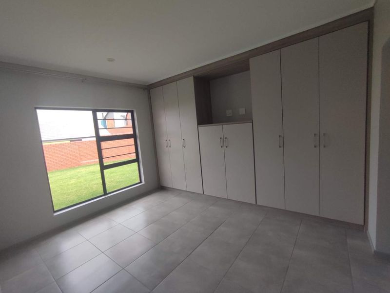 A bright, empty bedroom featuring modern tiled flooring and extensive built-in cupboard storage with a view of the rear garden.