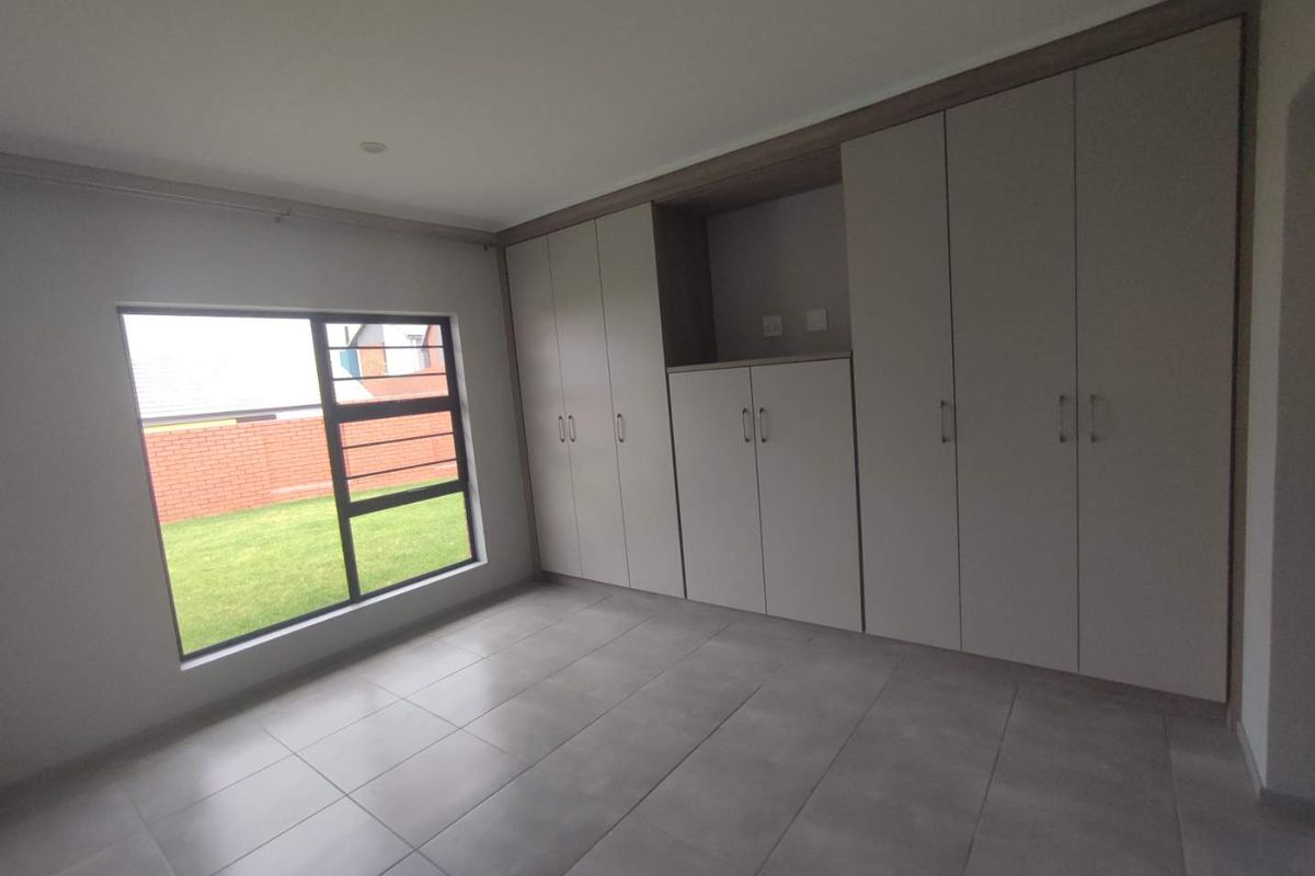 A bright, empty bedroom featuring modern tiled flooring and extensive built-in cupboard storage with a view of the rear garden.