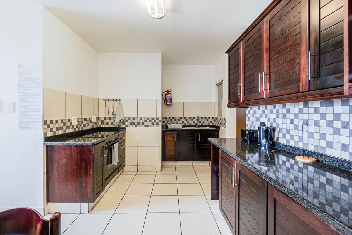 A functional kitchen featuring dark wood cabinetry, granite countertops, tiled splashbacks, and a built-in oven with a hob.