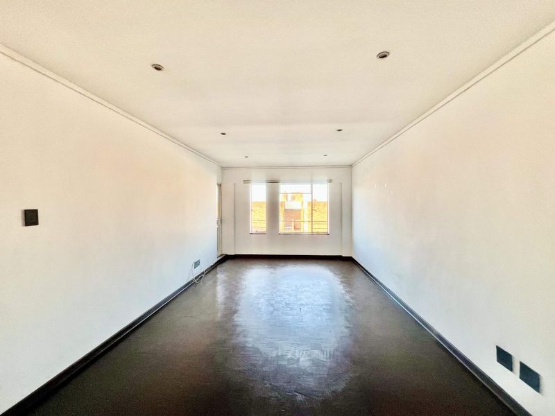 An empty, rectangular living area featuring recessed downlights, dark flooring, and natural light from a rear window.