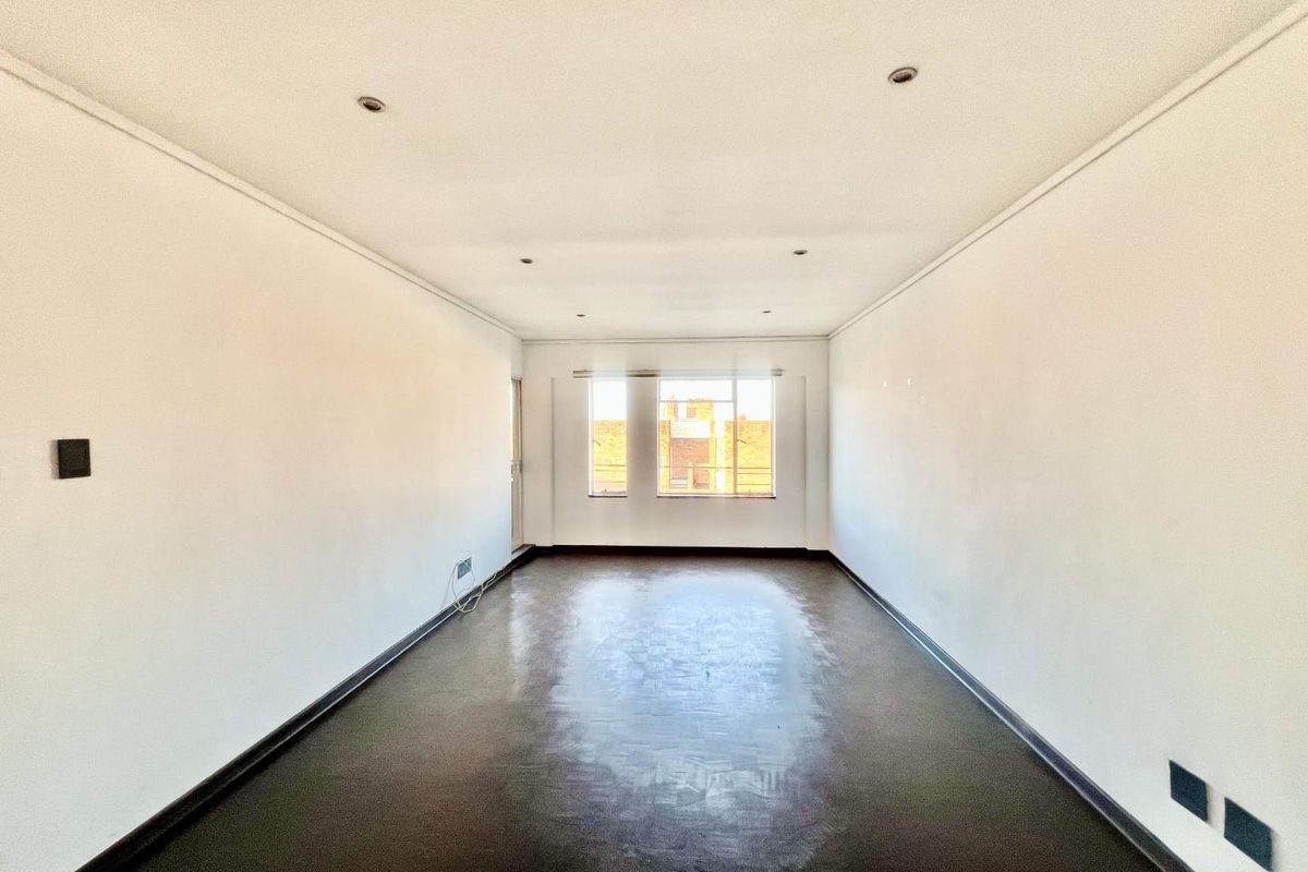 An empty, rectangular living area featuring recessed downlights, dark flooring, and natural light from a rear window.