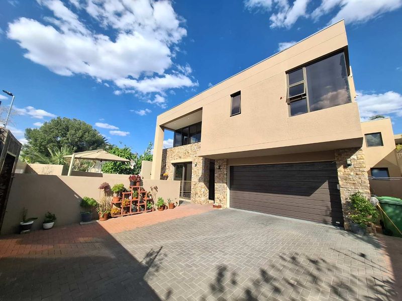 Modern two-story residential facade featuring stone cladding, stucco finish, a paved driveway, and a double garage door.