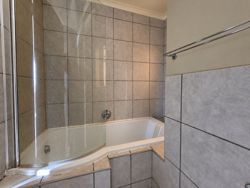 A functional bathroom featuring a built-in bathtub with a glass shower screen and neutral tiled wall finishes.