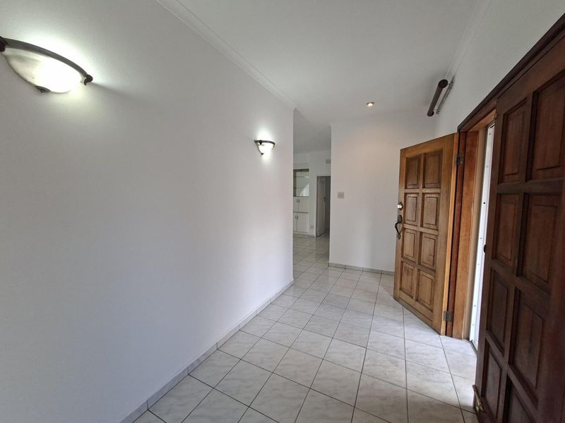 A bright and spacious entrance hall featuring neutral tiled flooring, wall-mounted lighting, and a classic solid timber panel front door.