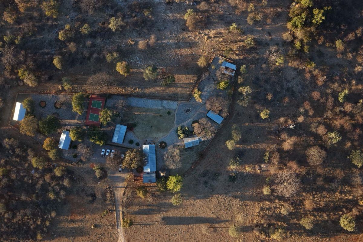 Aerial view of the lodge property featuring multiple structures, a tennis court, and established pathways set within a natural bushveld landscape.