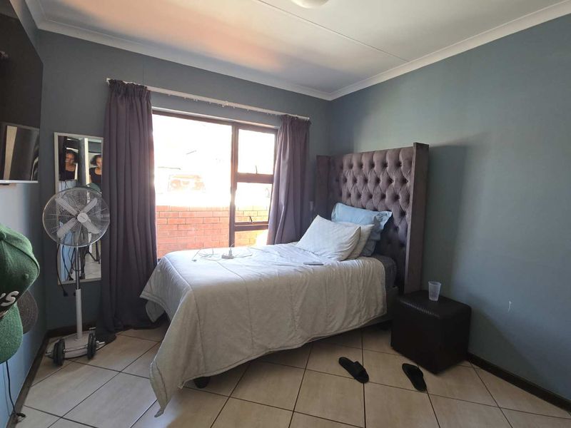 A functional bedroom featuring tiled flooring, a large window with natural light, and neutral wall finishes.