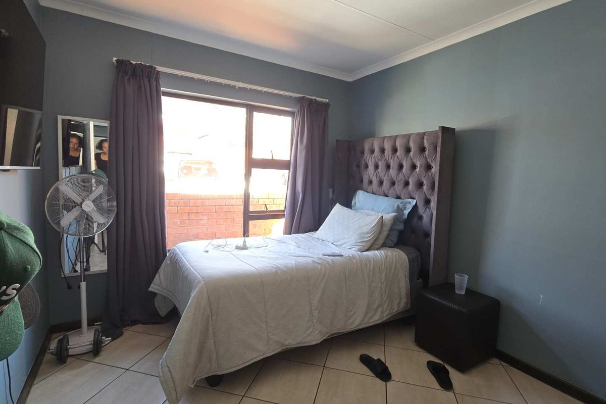 A functional bedroom featuring tiled flooring, a large window with natural light, and neutral wall finishes.