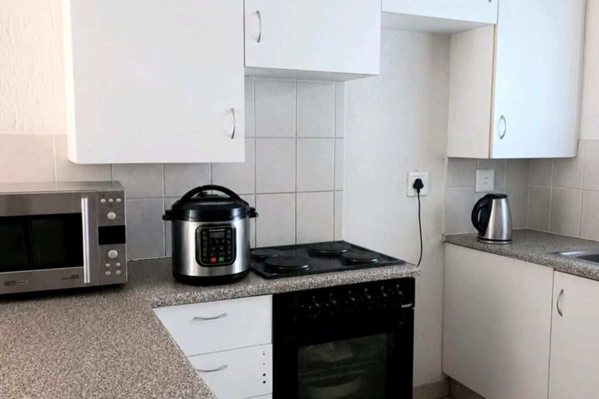 A functional kitchen featuring white cabinetry, granite-look laminate countertops, a tiled backsplash, and a built-in electric oven with a hob.