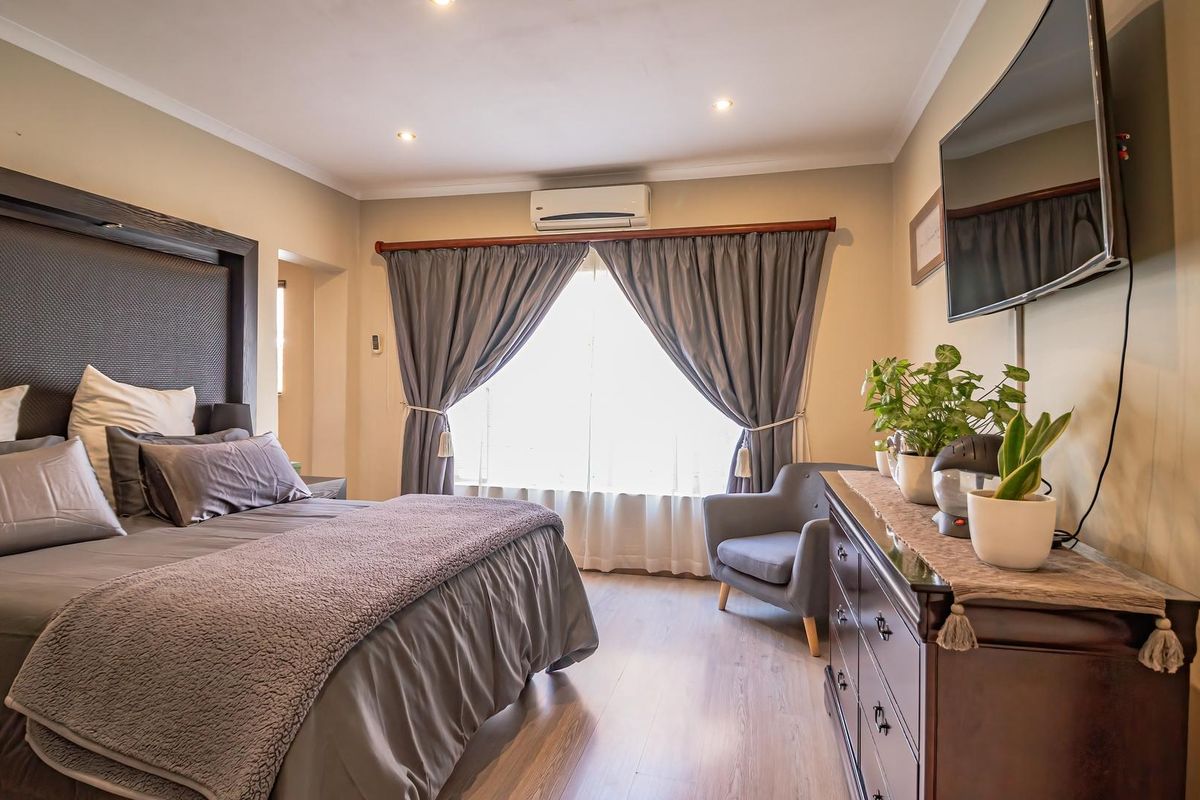 A well-maintained bedroom featuring laminate flooring, recessed downlighting, and a wall-mounted air conditioning unit, offering a comfortable and functional living space.