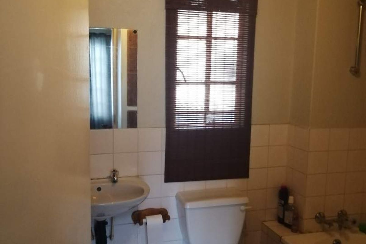 A functional bathroom featuring a pedestal basin, toilet, and bathtub with tiled finishes, offering potential for modernization and cosmetic updates.