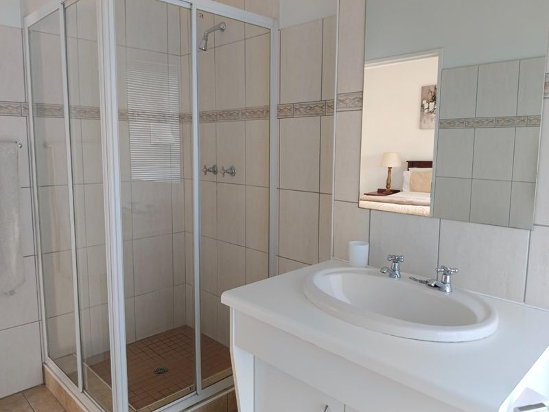 A functional bathroom featuring a glass shower enclosure, a vanity basin with a wall-mounted mirror, and neutral wall tiling.