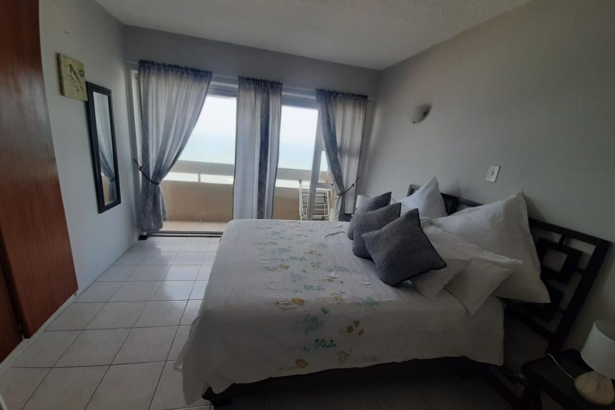 A bedroom featuring tiled flooring, built-in cupboards, and sliding glass doors that open onto a balcony with ocean views.