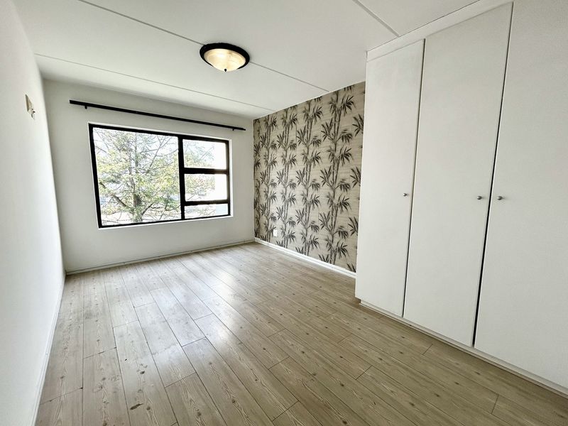 A bright, empty bedroom featuring modern laminate flooring, built-in cupboards, and a decorative feature wall, offering a clean and versatile living space.