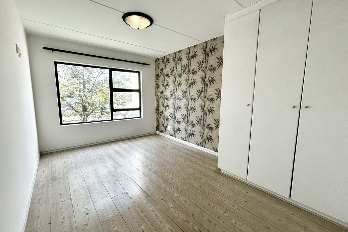 A bright, empty bedroom featuring modern laminate flooring, built-in cupboards, and a decorative feature wall, offering a clean and versatile living space.