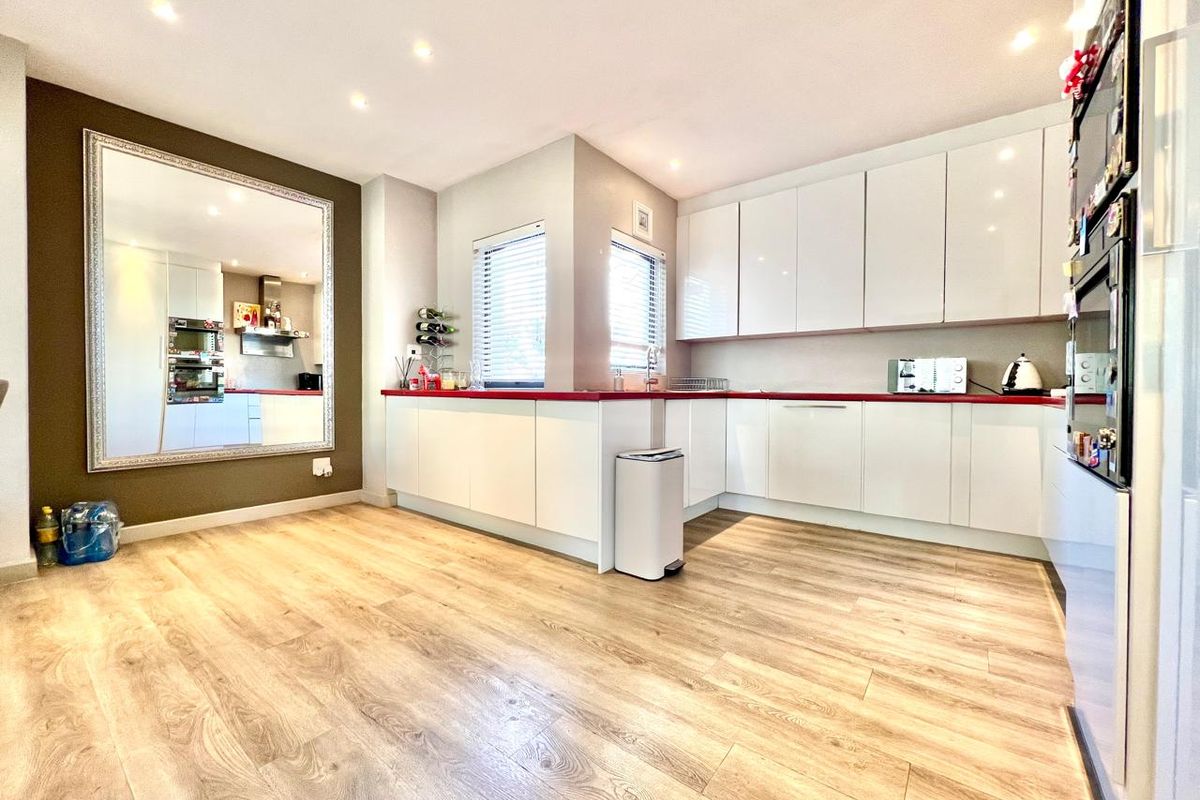 Modern kitchen featuring white high-gloss cabinetry, contrasting red countertops, integrated oven, and wood-look laminate flooring with recessed ceiling lighting.
