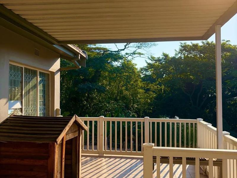 A covered outdoor patio featuring tiled flooring and protective railings, offering a functional space for relaxation with views of the surrounding greenery.