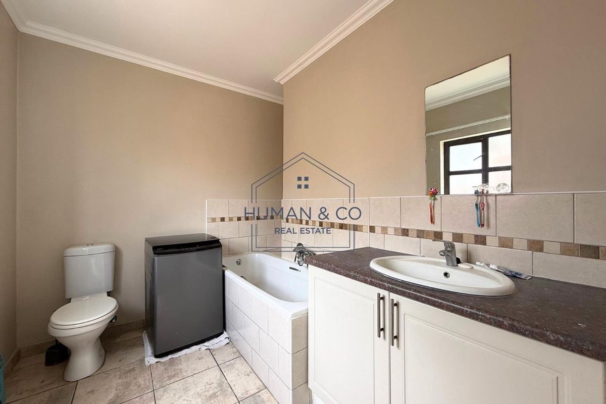 A functional bathroom featuring a built-in vanity with basin, a bathtub, and a toilet, finished with neutral wall tiles and floor tiling.