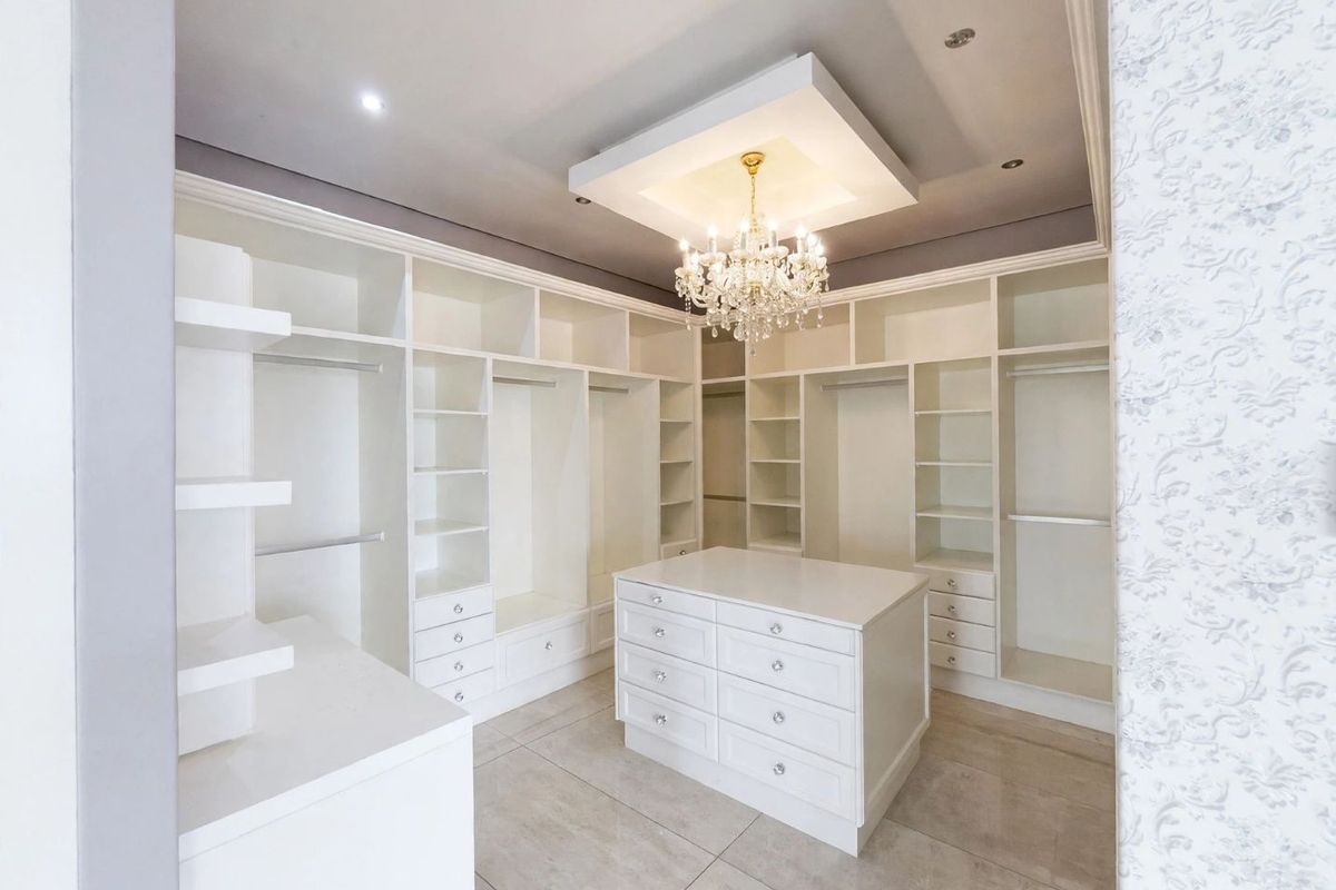 Spacious walk-in closet featuring extensive built-in cabinetry, a central storage island, tiled flooring, and elegant recessed ceiling lighting.