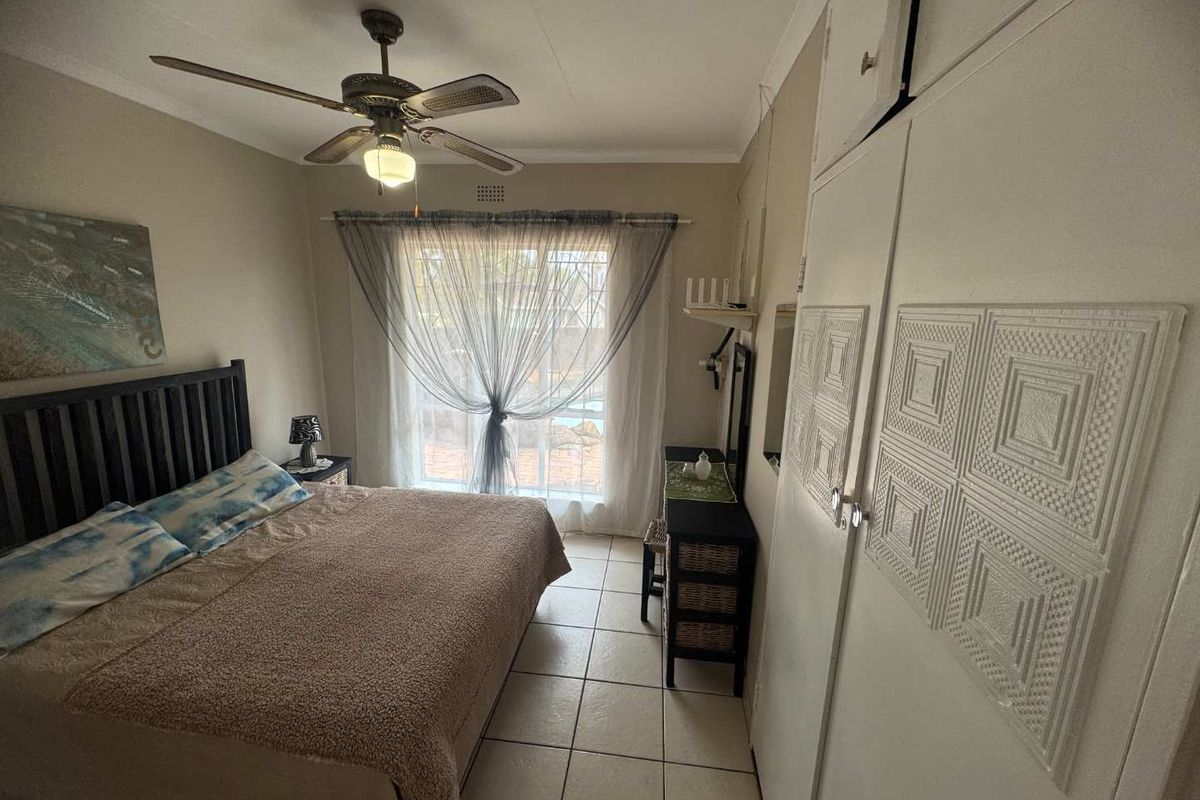 A bedroom featuring tiled flooring, a ceiling fan, and built-in cupboards with decorative paneling, providing direct access to the outdoor area.
