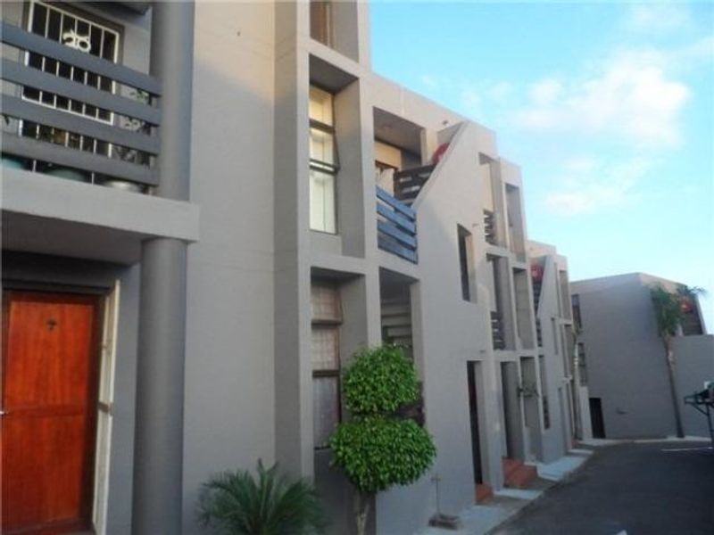 Exterior view of a modern apartment complex featuring concrete facade architecture, private balconies with railings, and a paved driveway entrance.
