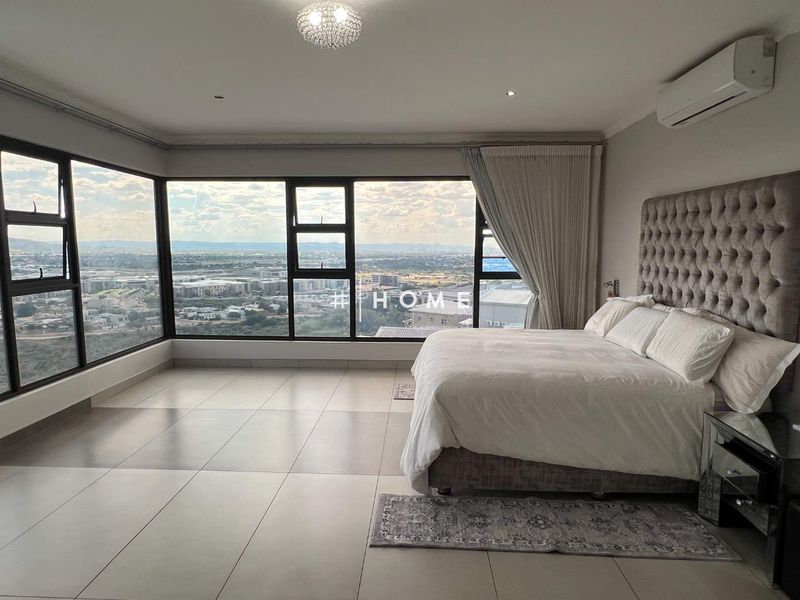 Spacious bedroom featuring large corner windows with expansive city views, tiled flooring, and a wall-mounted air conditioning unit.
