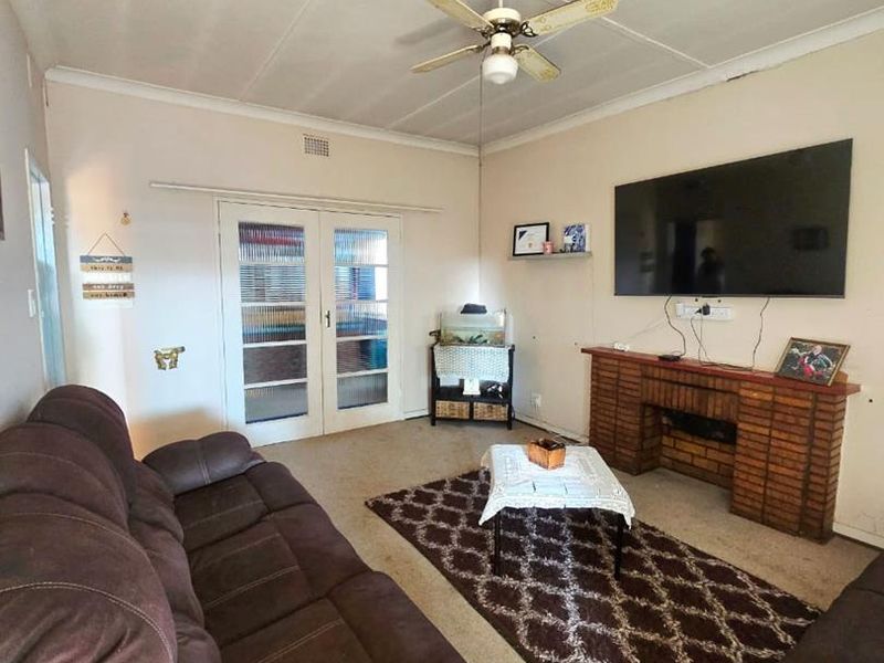 A living room featuring a brick fireplace, ceiling fan, and french doors leading to an adjacent space, with neutral wall finishes.