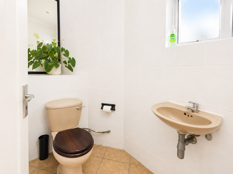 A compact guest bathroom featuring tiled walls, a wall-mounted basin, and a toilet with a wooden seat.